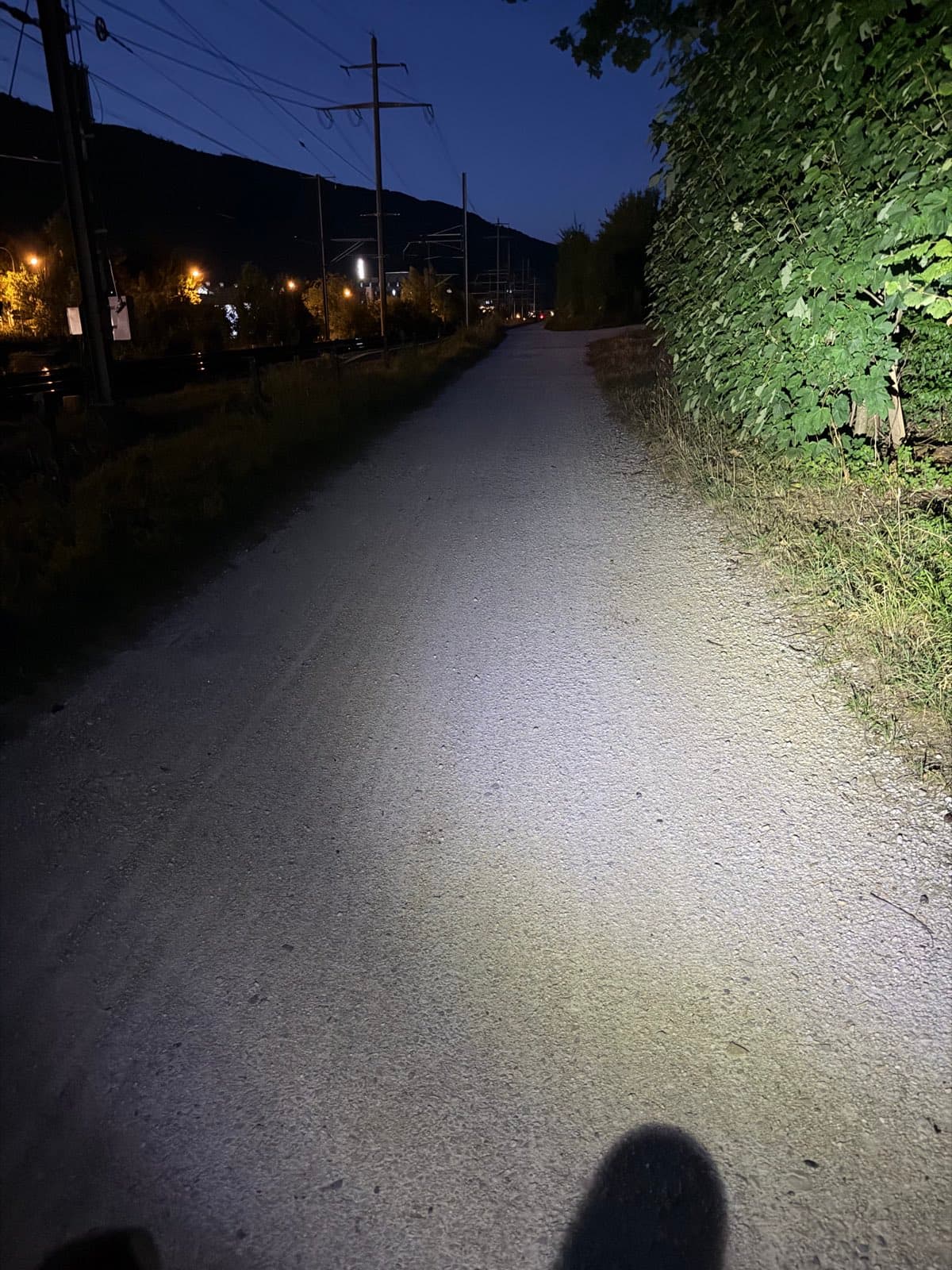 Kiesweg im Lichtkegel der Velolampe, Strassenlaternen in der Ferne